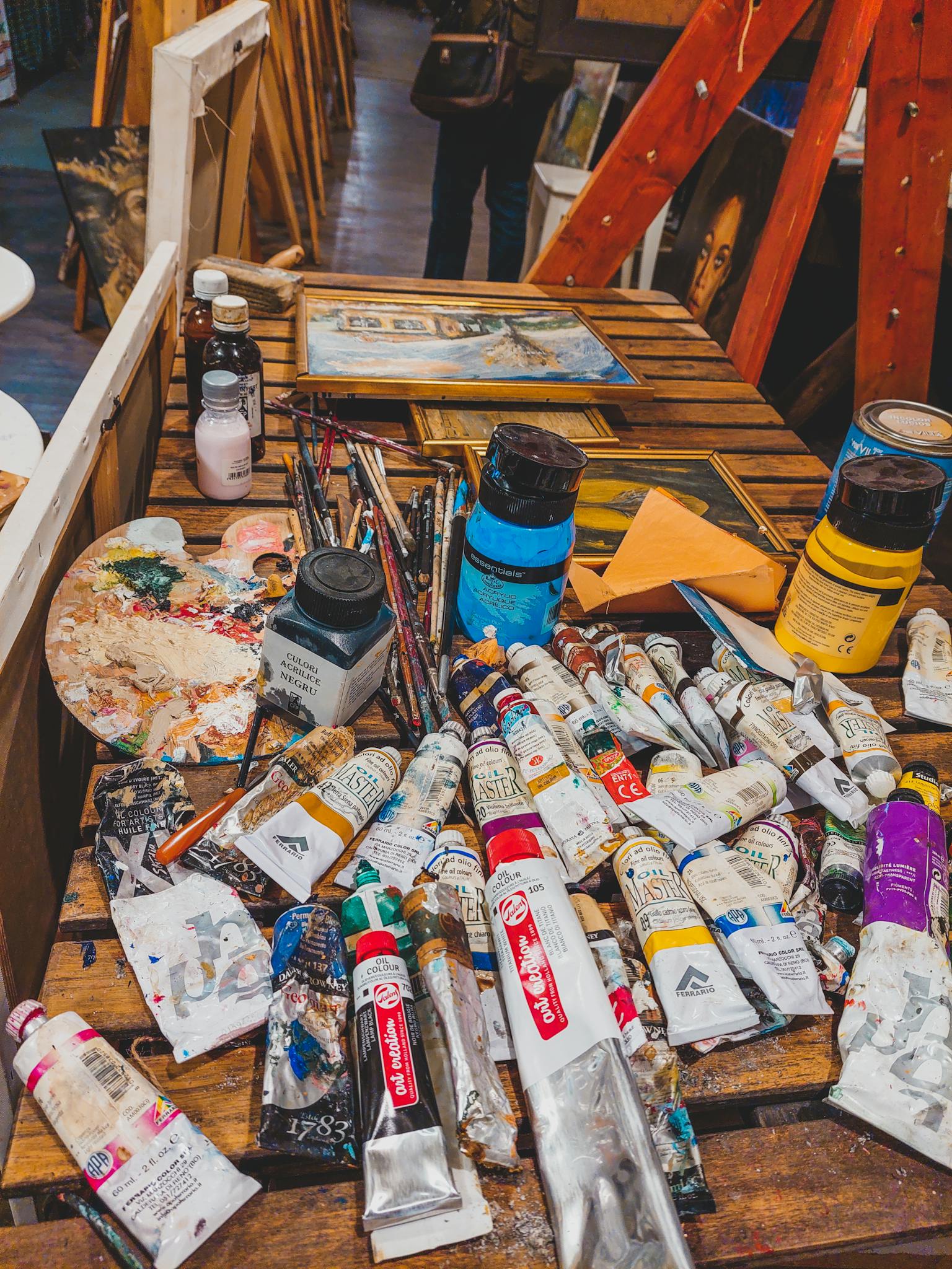 A variety of paints and brushes displayed on a wooden table in an art studio.