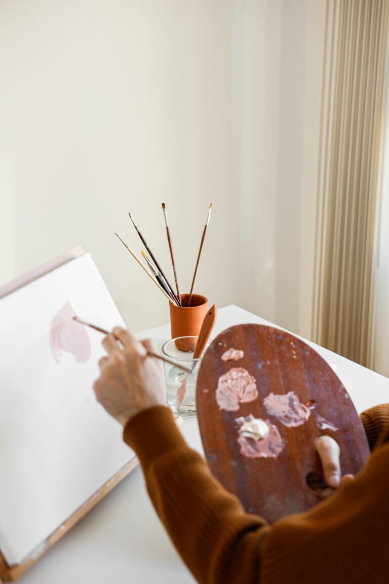 Artist holding a palette and painting on canvas in a bright, creative indoor studio.